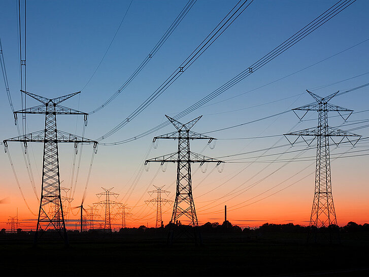 Strommasten bei Sonnenuntergang, am Horizont Windräder Strommasten bei Sonnenuntergang mit Windrädern am Horizont